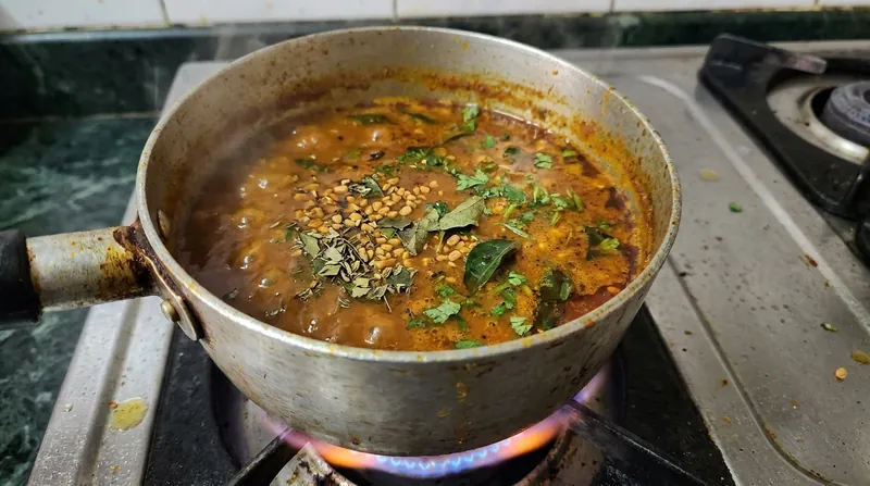 Un curry aromático en una cazuela con especias visibles, incluido el fenogreco, sobre fuego suave