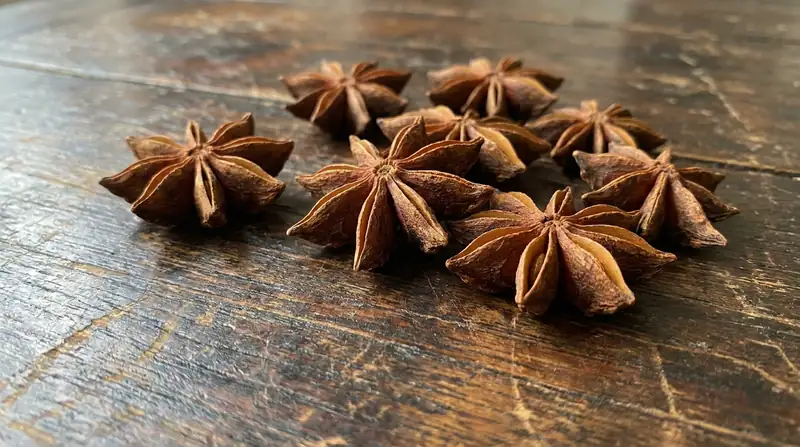 Varias estrellas de anís estrellado enteras sobre una superficie de madera oscura, con textura muy detallada